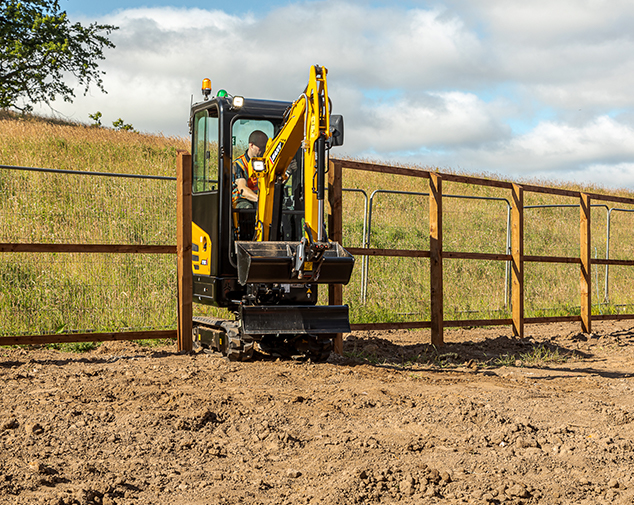 SY18C excavator fitting through a small opening in a fence